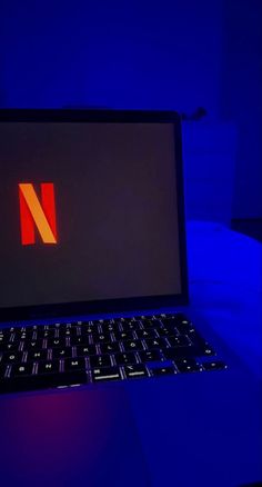 an open laptop computer sitting on top of a blue lit desk in a dark room