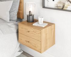 a nightstand with a lamp on top of it next to a bed and framed artwork