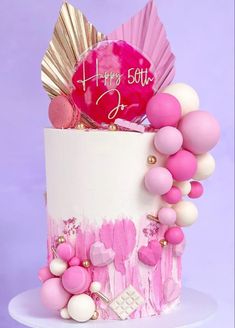 a pink and white birthday cake decorated with balloons, confetti and seashells