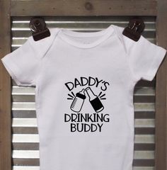 Daddy's Drinking Buddy baby bodysuit. This bodysuit is a perfect baby shower gift and sure to get a laugh. *Bodysuits are Carter's brand. Please see their sizing chart if you aren't sure what size to order. *All bodysuits are white. The color you choose is for the text/image. *If you would like a colored bodysuit, please request a custom order and we can see if we can meet your needs. Please note though that there is usually an added charge for this. *We are also able to do t-shirts. If interest Family Matching Onesie With Funny Text For Birthday, Family Matching Birthday Onesie With Funny Text, Short Sleeve Onesie With Funny Text For Birthday, Father's Day Cotton Onesie With Graphic Print, Funny Text Short Sleeve Onesie For Birthday, Father's Day Casual Short Sleeve Onesie, Casual Short Sleeve Onesie With Funny Text For Birthday, Funny Short Sleeve Onesie For Birthdays, Funny Short Sleeve Onesie For Birthday