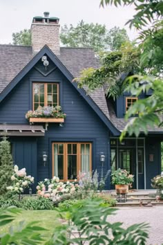 a blue house with lots of windows and flowers in the front yard, surrounded by greenery