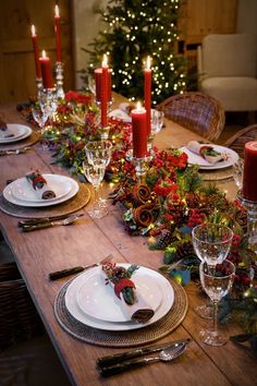 the table is set for christmas dinner with candles and greenery on each place setting