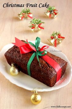 christmas fruit cake on a white plate with red ribbon and bells around the edge, sitting on a wooden table