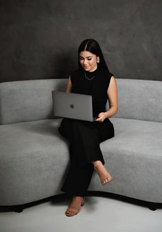 a woman sitting on top of a gray couch using a laptop computer in her lap