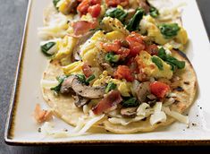 two tortillas on a white plate topped with eggs, tomatoes and spinach