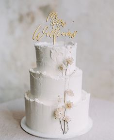 a three tiered white cake with flowers on the top and bottom, sitting on a table