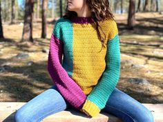 a woman is sitting on a log in the woods wearing a colorful sweater and jeans