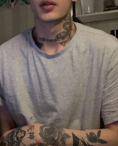 a young man with tattoos on his arms and chest is looking at the camera while wearing a grey t - shirt