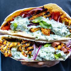 two tacos with meat, vegetables and sauce on them are held in someone's hand