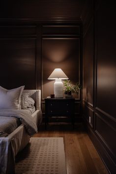 a bed sitting next to a night stand with a lamp on top of it in a bedroom