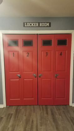 two red doors with numbers on them in front of a gray wall and wooden floor