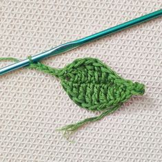 a green crochet piece next to a knitting needle