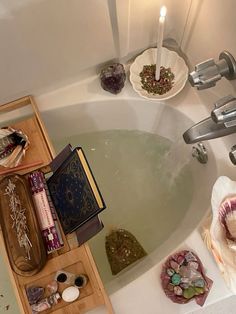 a bath tub filled with lots of different items next to a candle and some books