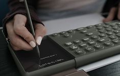 a person is writing on a keyboard with a pen in their left hand, while holding a notebook