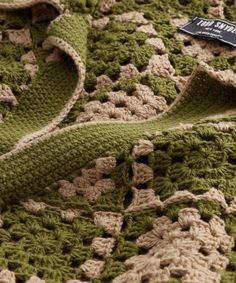 a crocheted green and beige blanket with a tag on it's side