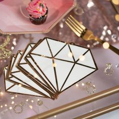 a table topped with pink cupcakes and gold foiled utensil holders