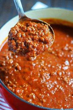 a ladle full of chili sauce with a spoon in it