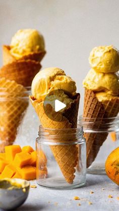 three ice cream cones in glass containers with mango slices and orange peels around them