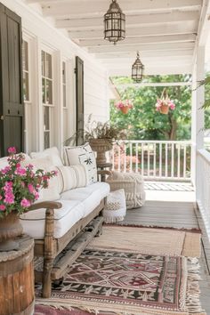 a porch with white furniture and pink flowers on the rugs, hanging from the ceiling