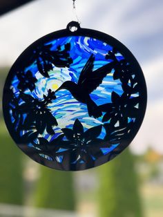 a glass ornament hanging from a window with trees and sky in the background