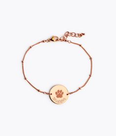 a gold bracelet with a dog paw charm on the front and an engraved disc that says,