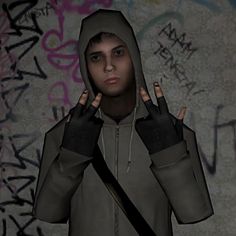 a man in grey hoodie holding two fingers up to his face with graffiti on the wall behind him