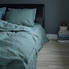 a bed with green sheets and pillows in a room next to a stack of books