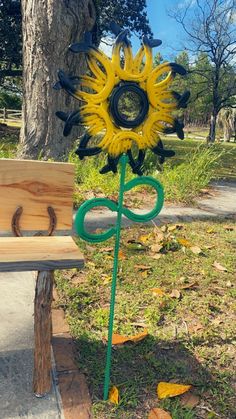 a yellow sunflower sculpture sitting on top of a wooden bench next to a tree