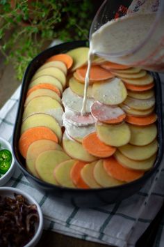 a person pouring dressing on some food in a pan with other foods and vegetables around it