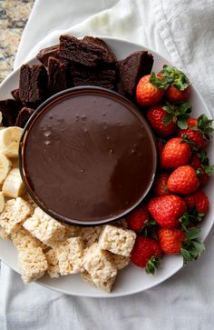 a white plate topped with chocolate and strawberries next to crackers, bananas and other snacks