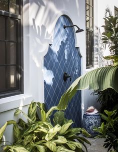 a blue and white fountain in front of a house with potted plants next to it