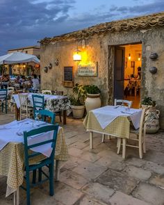 an outdoor dining area with tables, chairs and umbrellas at dusk in front of a stone building