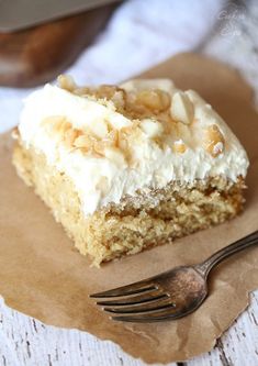 a piece of cake with white frosting and nuts on top is sitting on a napkin next to a fork