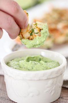 a person dipping guacamole into a white bowl