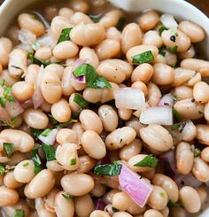 a white bowl filled with beans, onions and cilantro on top of a wooden table