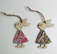 two wooden rabbits are hanging from twine with floral print dresses and flowers on them