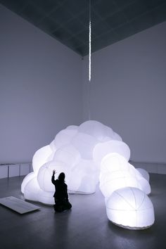 a person sitting on the floor in front of a large white cloud shaped object with lights hanging from it's ceiling