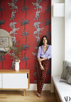 a woman standing in front of a red wallpapered room with an animal pattern