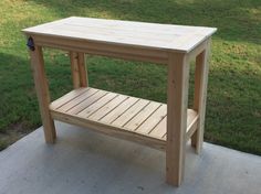 a small wooden table sitting on top of a cement floor next to a grassy field