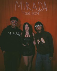 three people standing next to each other in front of a red wall with the words mirada tour written on it