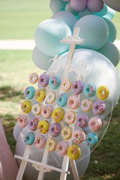 there is a sign with donuts on it and balloons in the back ground behind it