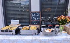 a buffet table set up with food and wine glasses on it, near a window