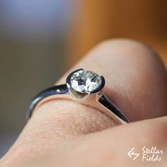 a close up of a person's hand holding a ring with a diamond on it