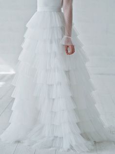 a woman in a white wedding dress with sheer sleeves and long ruffles on the skirt