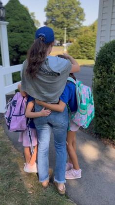 two girls are hugging each other on the side walk with their back to the camera