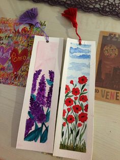 two bookmarks with flowers painted on them sitting on a table next to a lace doily