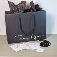 a black shopping bag sitting on top of a table next to a bottle of wine