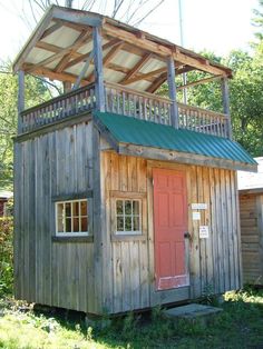 a small wooden building with a green roof and red door in the grass next to trees