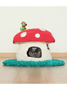 a black cat sitting in a crocheted mushroom house with a green frog on top