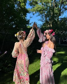 two women in dresses are standing on the grass and one is holding her hand up